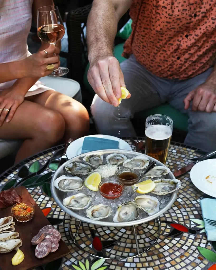 Hands squeezing lemon over fresh oysters, charcuterie, and drinks.