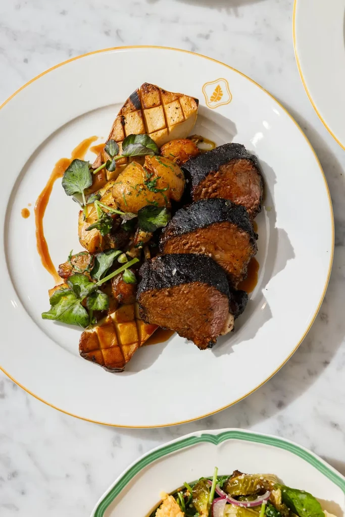 Seared meat, roasted potatoes, grilled mushroom, and greens on a white plate.