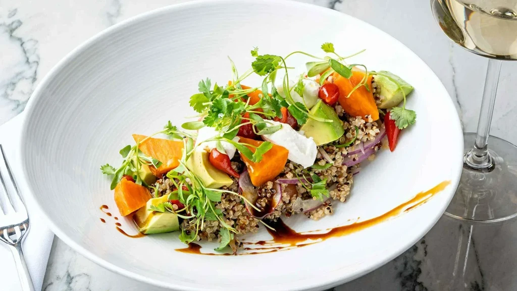 Vibrantly plated grain bowl with quinoa, avocado, vegetables, and creamy cheese.