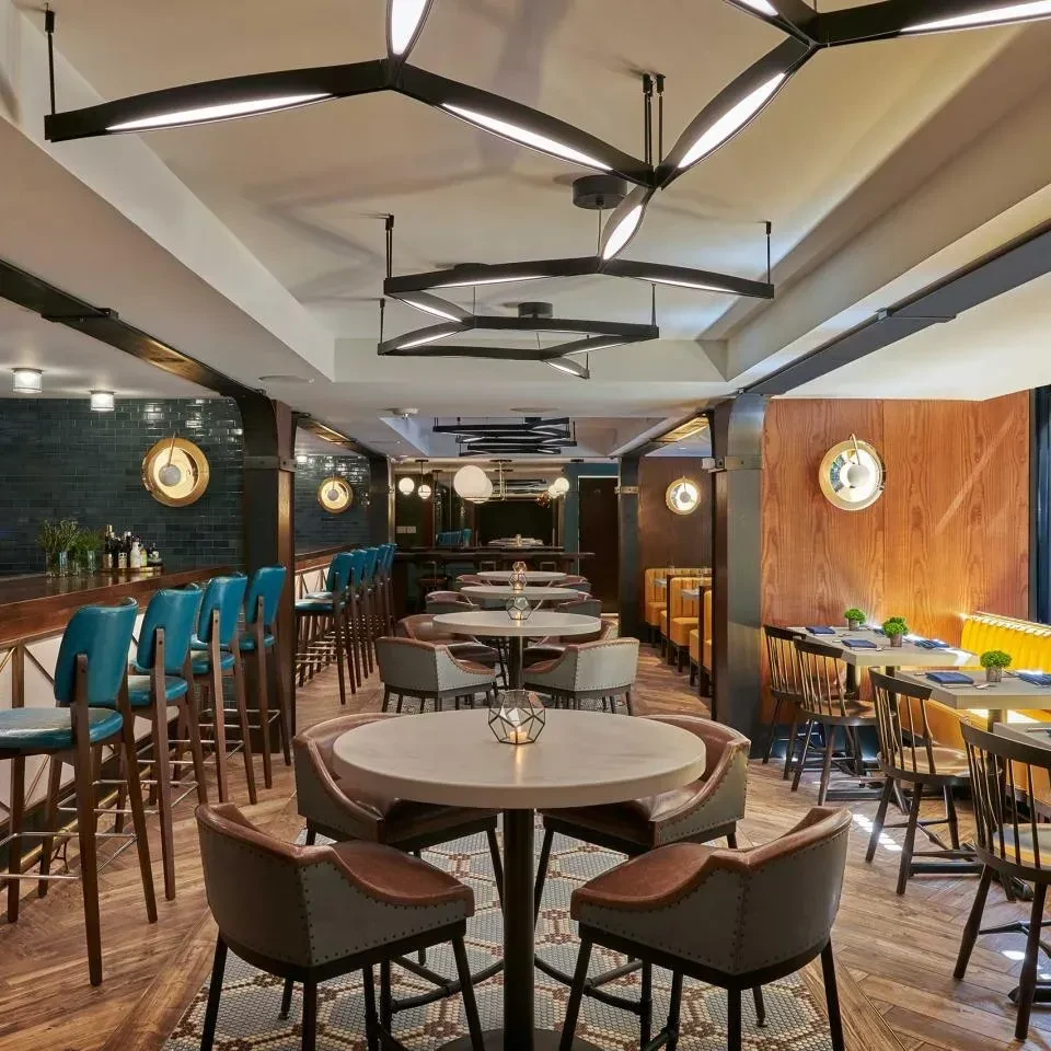 Empty modern restaurant interior with a bar, diverse seating, and geometric lights.
