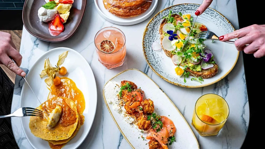 Overhead shot of hands cutting brunch food on a marble table.