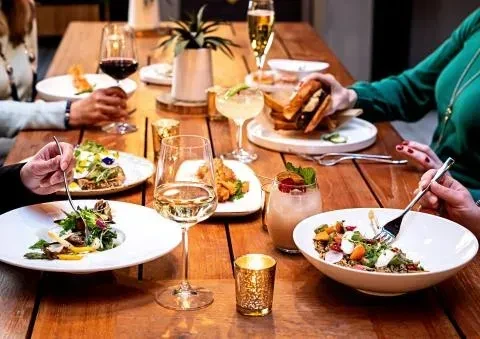 Elevated view of a warm dining scene with food, drinks, and hands.