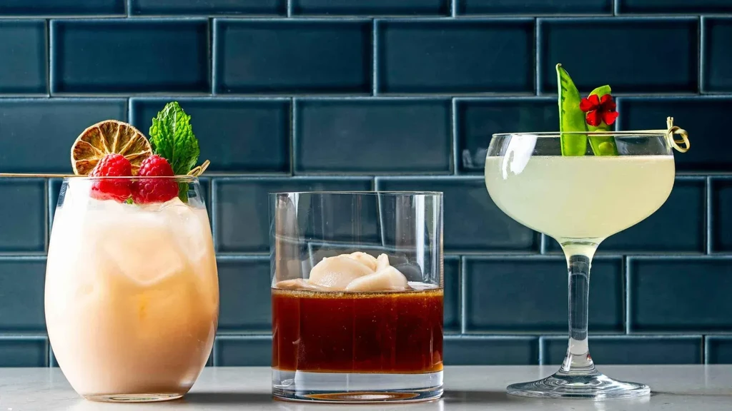 Three garnished cocktails on a bar against a dark subway tile wall.