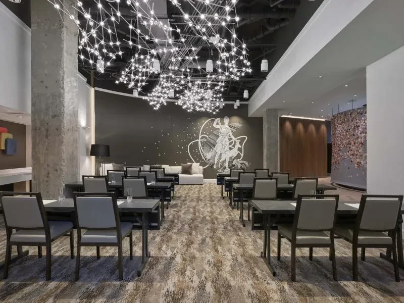 Modern restaurant with square tables, elaborate chandelier, concrete pillars, classical mural.