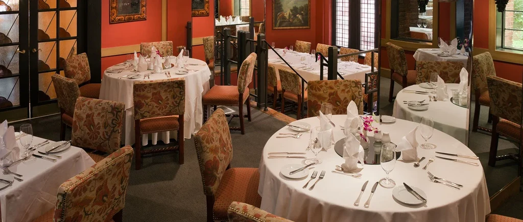 Formal restaurant dining room with set tables, purple orchids, ornate decor.