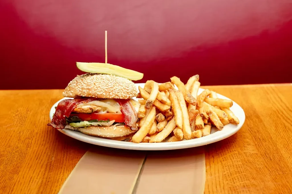 Close-up of a high-stacked burger, fries, and pickle spear on a plate.