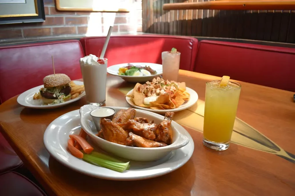 Restaurant table with chicken wings, burger, nachos, milkshake, and drinks.