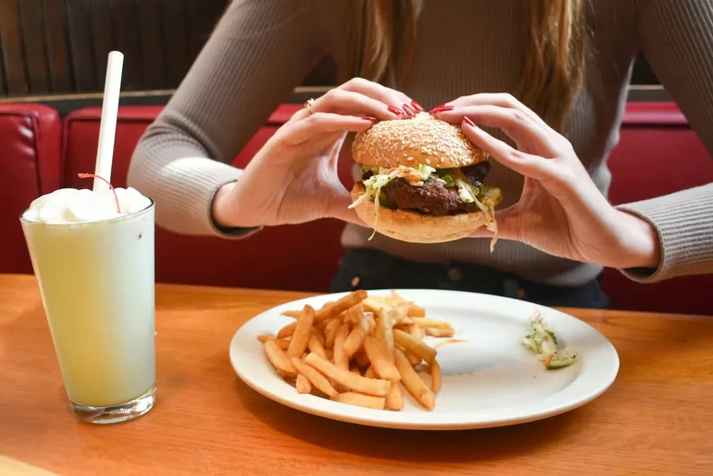 Hands holding a burger, fries, and green milkshake at a diner.