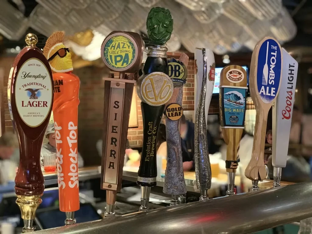 A close-up of diverse beer tap handles at a bustling bar.