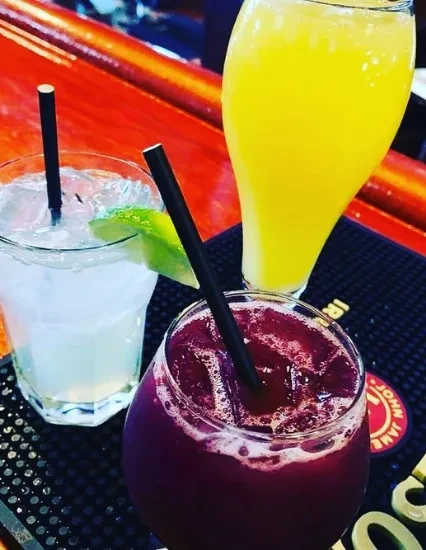 Three vibrant drinks on a shiny bar counter.