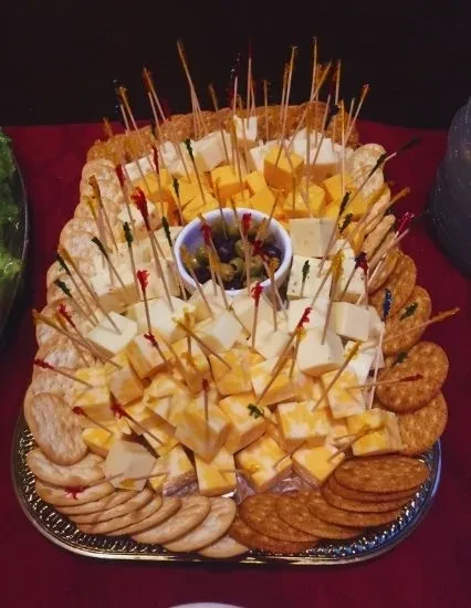 Silver platter with cubed cheeses, crackers, and olives with toothpicks.