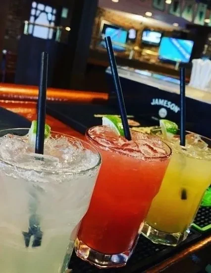 Three vibrant green, red, yellow cocktails on a bar.