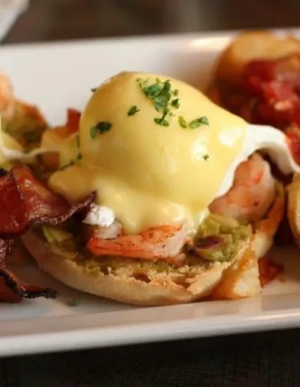 Open-faced English muffin with shrimp, avocado, poached egg, hollandaise, and bacon.