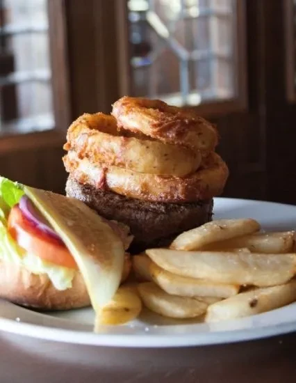 Hamburger with onion rings on patty, served with french fries.
