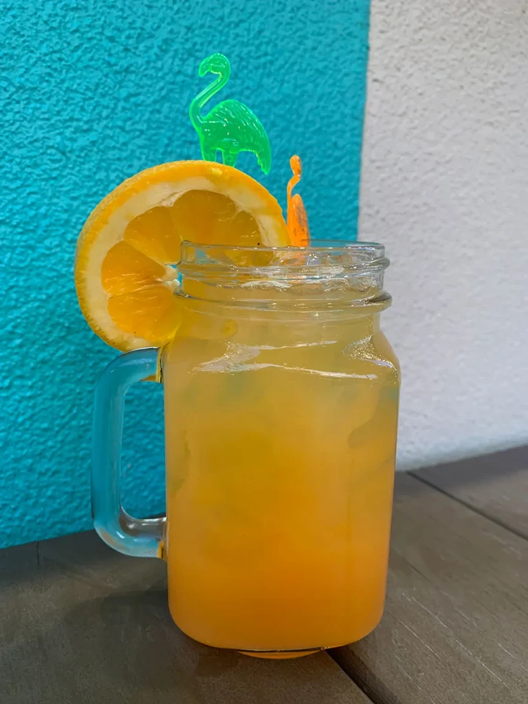 Mason jar with yellow-orange drink, orange slice, and flamingo pick.