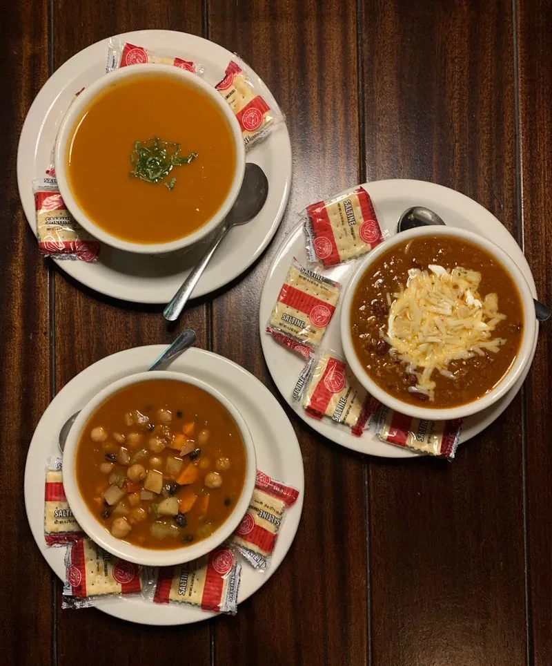 Overhead view of three bowls: orange soup, vegetable stew, and chili.