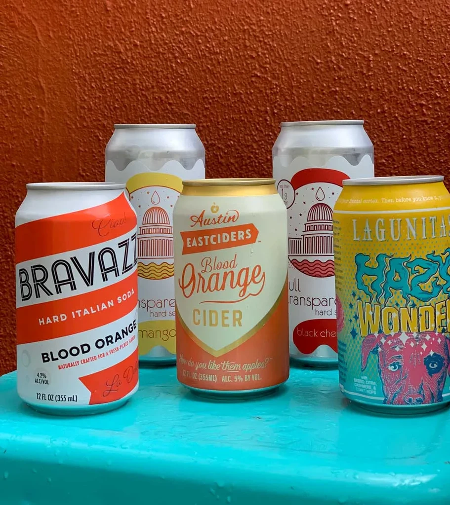 Five cold beverage cans: soda, cider, beer, and two hard seltzers.