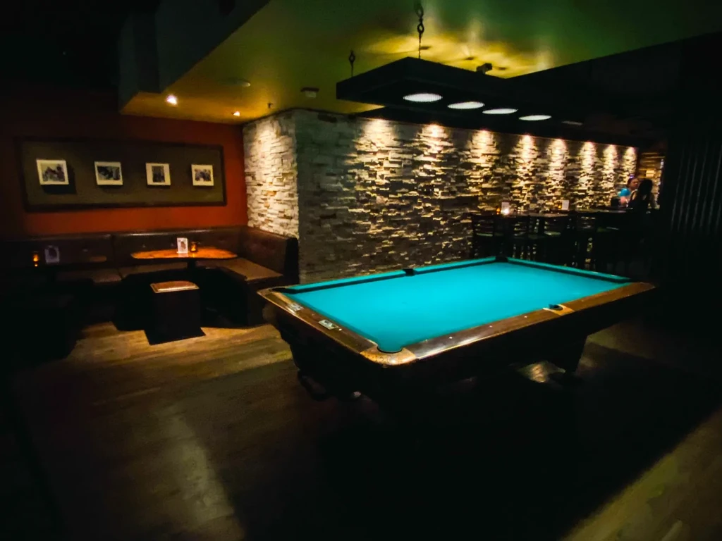 Teal pool table in a dimly lit bar with booths and a stone wall.