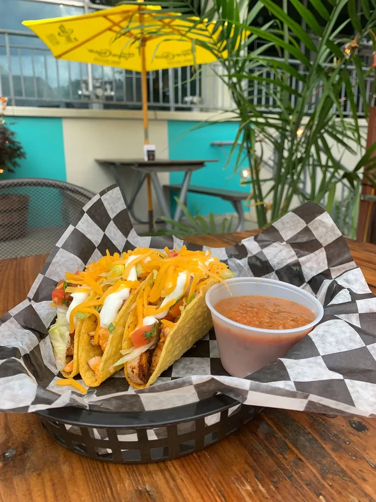 Three fully loaded tacos and salsa on a rustic outdoor table.