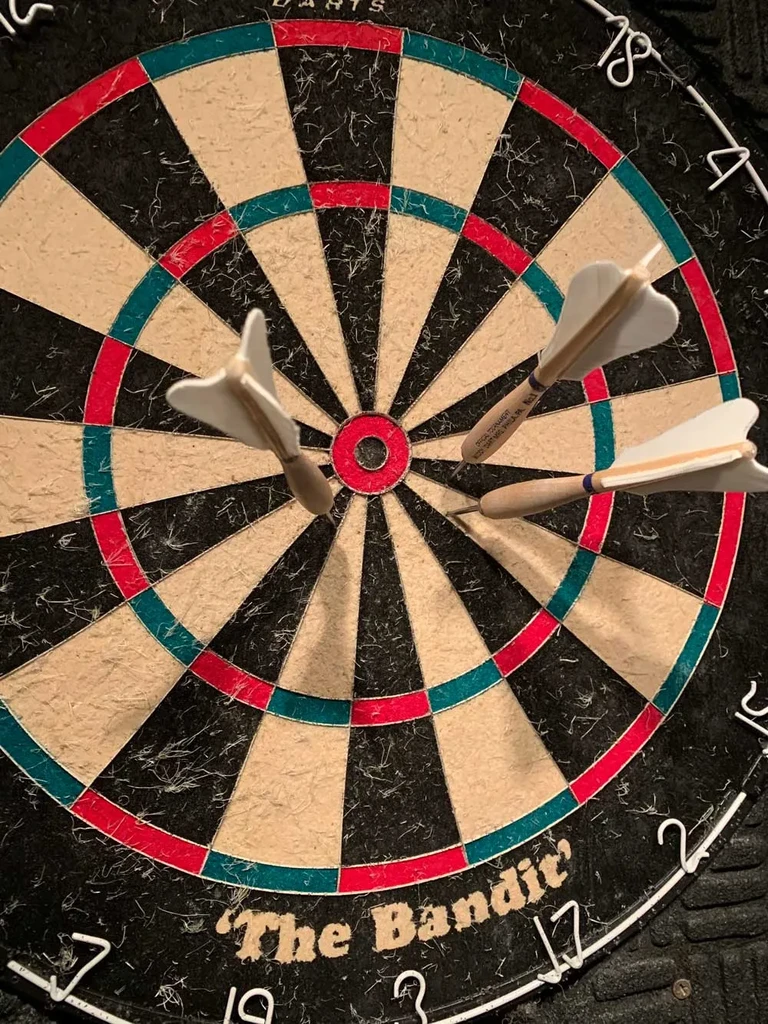 Traditional 'The Bandit' dartboard with three white darts, showing use.