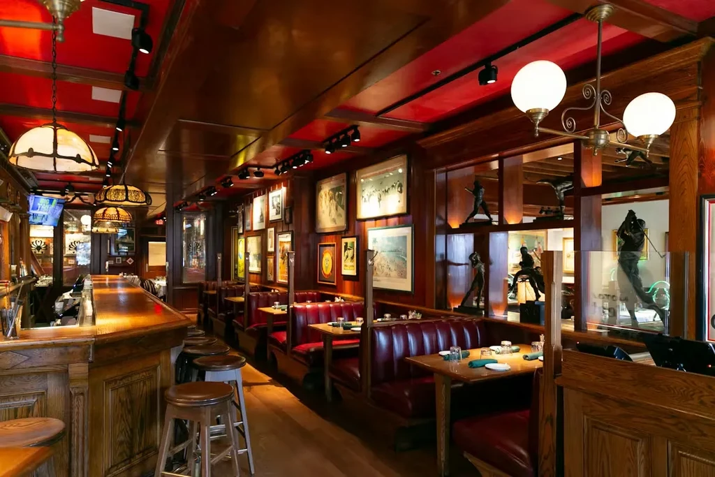 Restaurant interior with wooden bar, red booths, dark wood, and framed art.