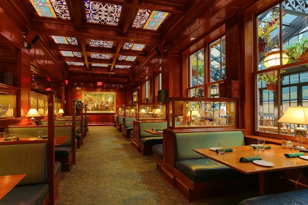 Luxurious restaurant interior with dark wood, stained glass, and empty green booths.