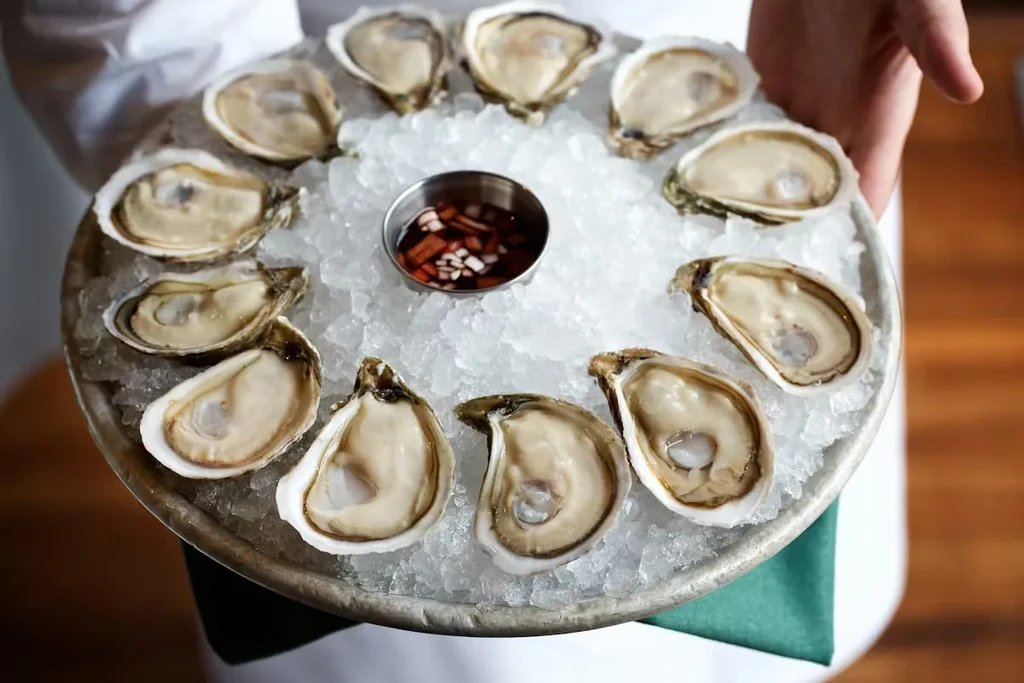 A dozen oysters on the half shell with sauce, on crushed ice.