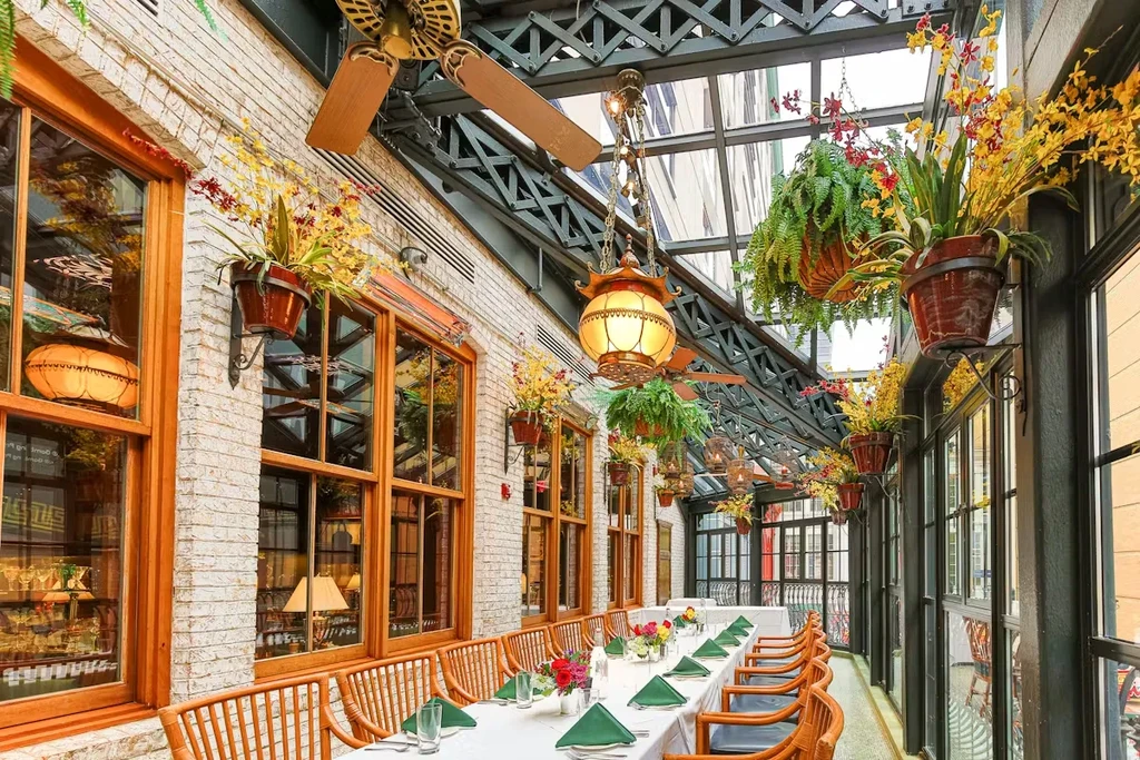 Enclosed restaurant patio with glass ceiling, potted plants, and set dining table.