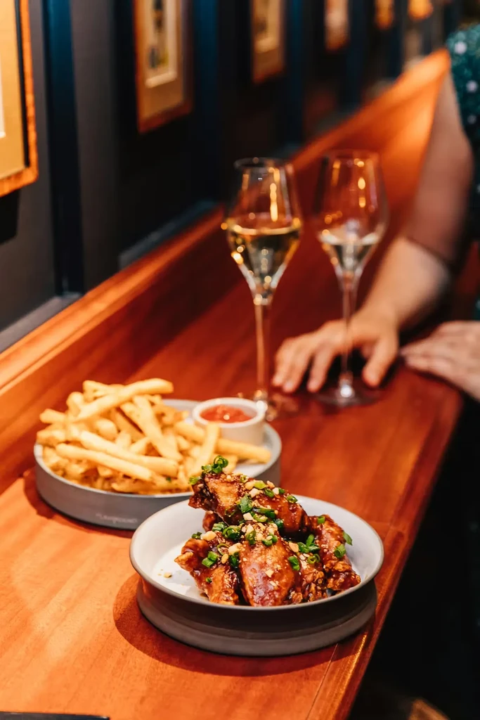 Glazed chicken wings, fries, and champagne flutes on a wooden bar.