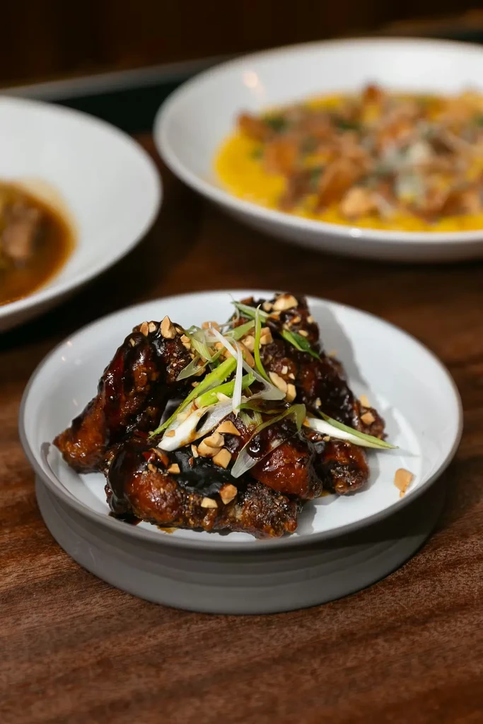 Dark, glossy chicken wings with peanuts and green onions in a bowl.
