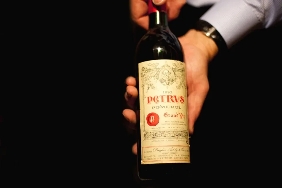 Hands hold a dark bottle of 1993 Petrus Pomerol wine.