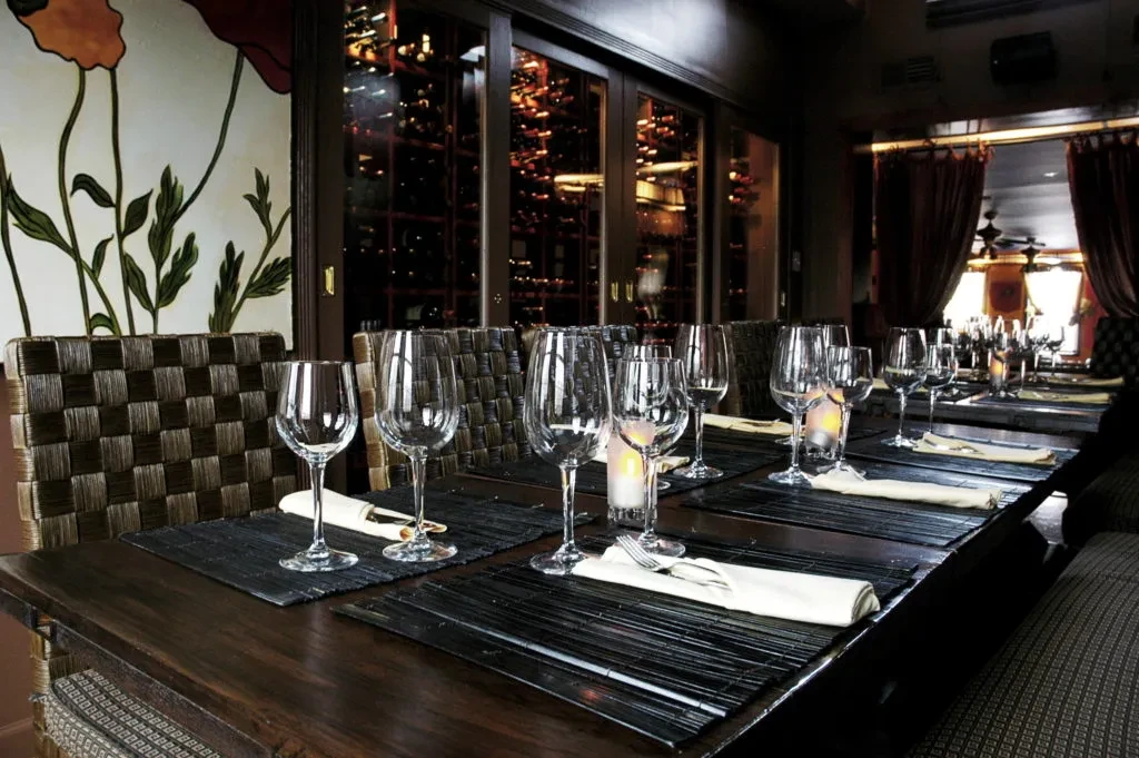 Restaurant interior: set table, glass wine cellar, and modern poppy mural.