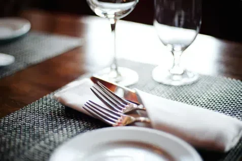 Neatly arranged place setting with wrapped silverware on a dark placemat.