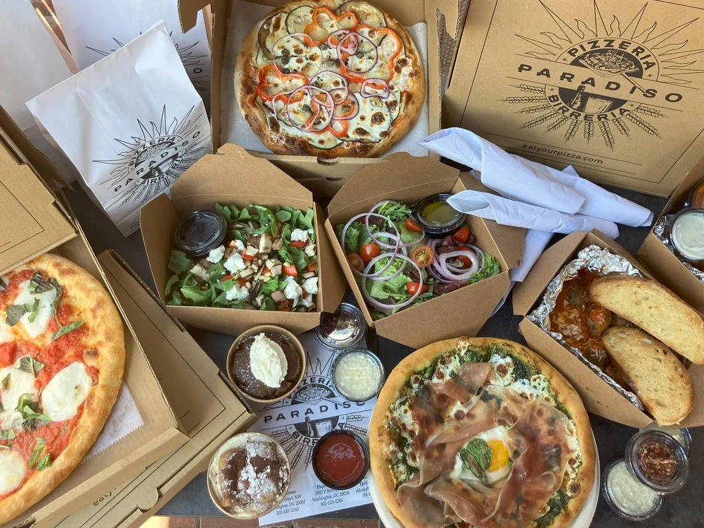 Pizzeria Paradiso takeout spread: three pizzas, salads, meatballs, and desserts.