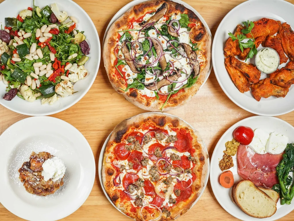 Overhead view of six diverse dishes: salads, pizzas, wings, charcuterie, and dessert.