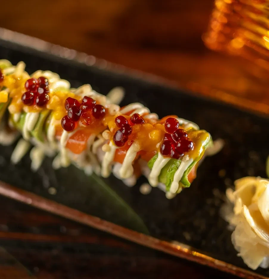 Close-up of uramaki sushi with avocado, red roe, sauces on dark plate.