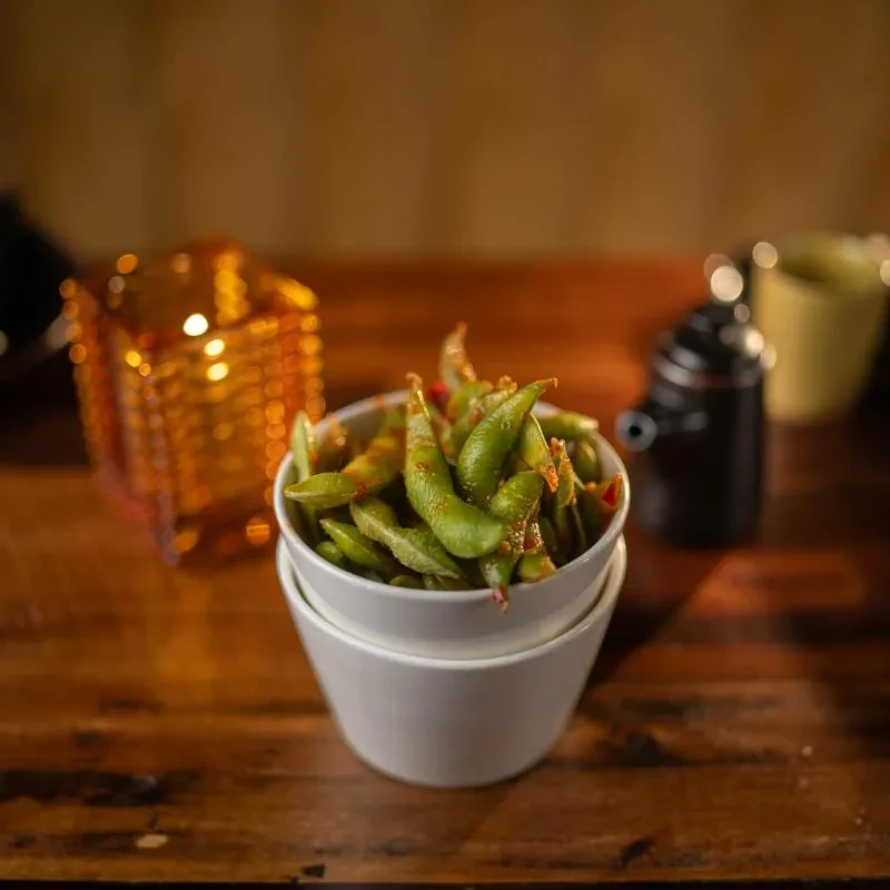 Stacked white bowls, top bowl filled with chili-seasoned edamame.