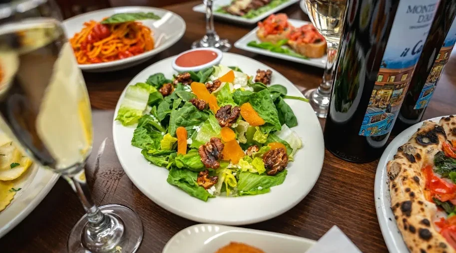 Vibrant restaurant table with salad, wine, spaghetti, and pizza.