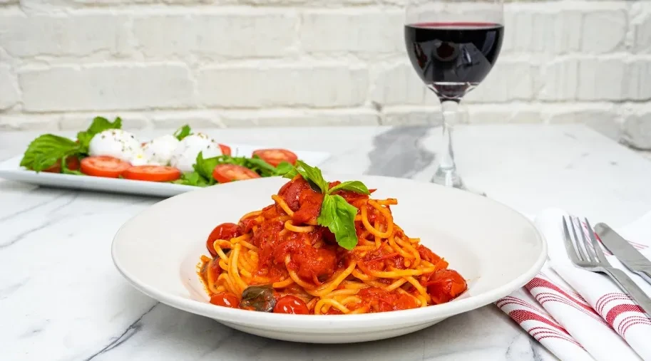 Italian spaghetti, red wine, and Caprese salad on a marble table.