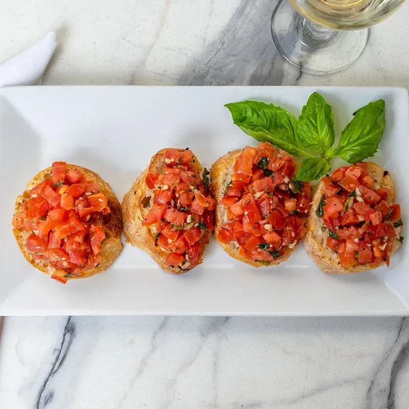 Four bruschetta with tomatoes, basil, wine glass, and napkin.