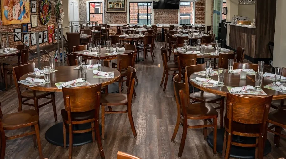 Empty restaurant interior with wooden tables, brick walls, bar, and staircase.