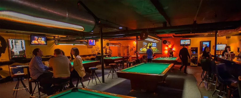 Dimly lit pool hall bar with patrons playing and socializing.