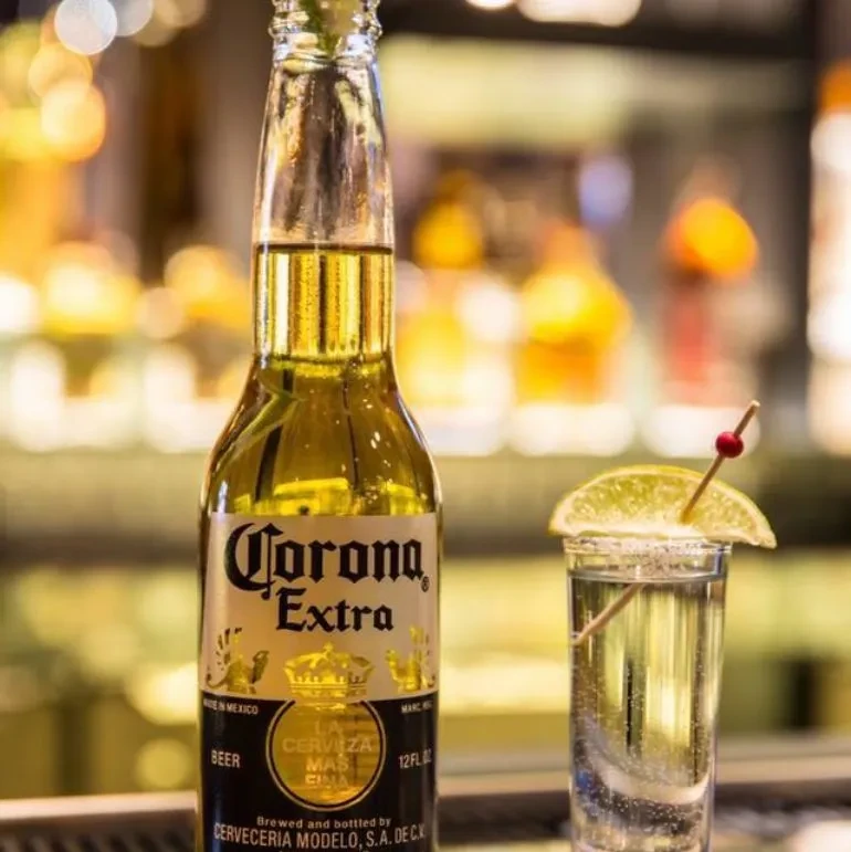 Corona Extra bottle and lime-garnished shot glass on a bar.