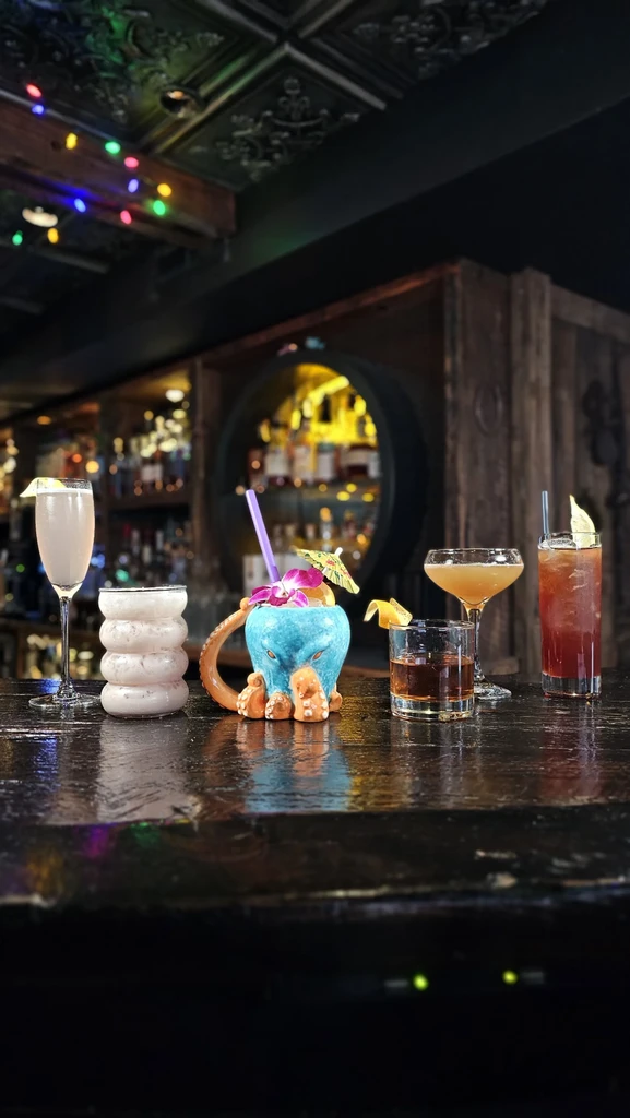 Five distinct, colorful cocktails on a dark bar counter.