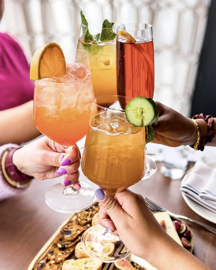 Diverse hands clinking four different colorful cocktails.