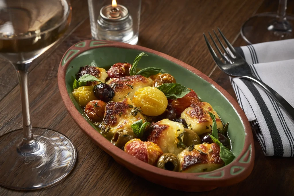Plated gnocchi or potatoes with tomatoes, olives, basil, wine, and candle.