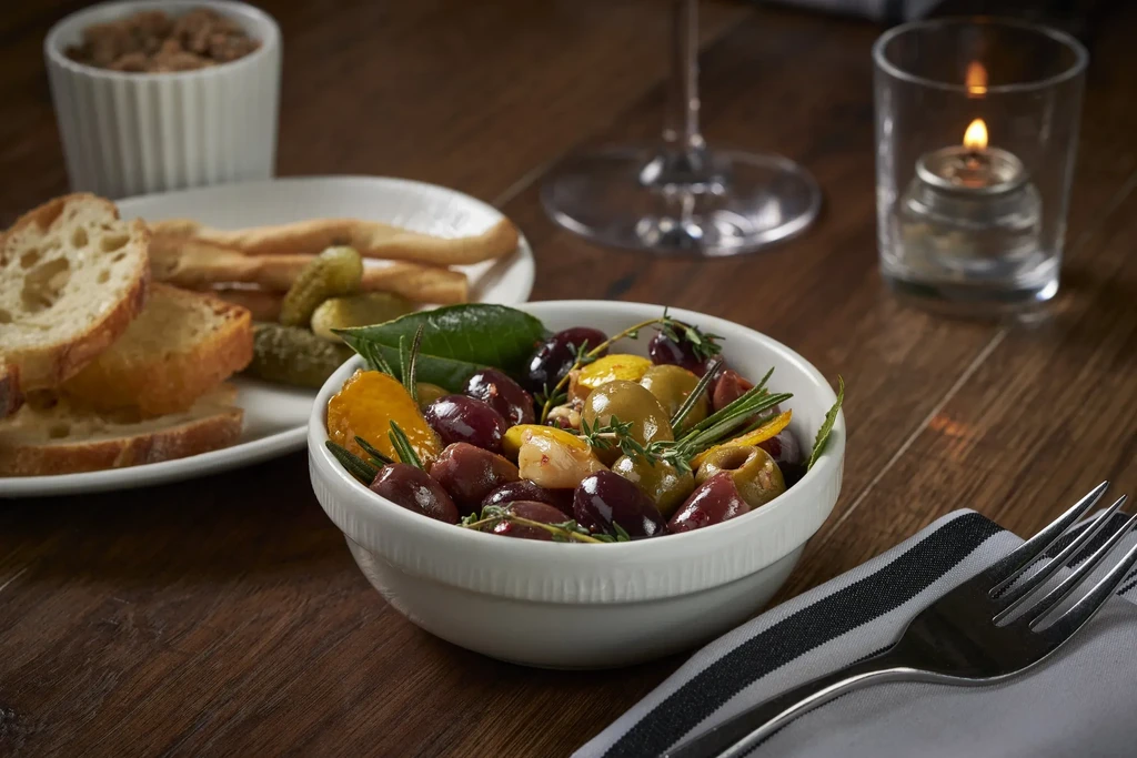 Colorful marinated olives with rosemary, bread, pickles, and a lit tea light.