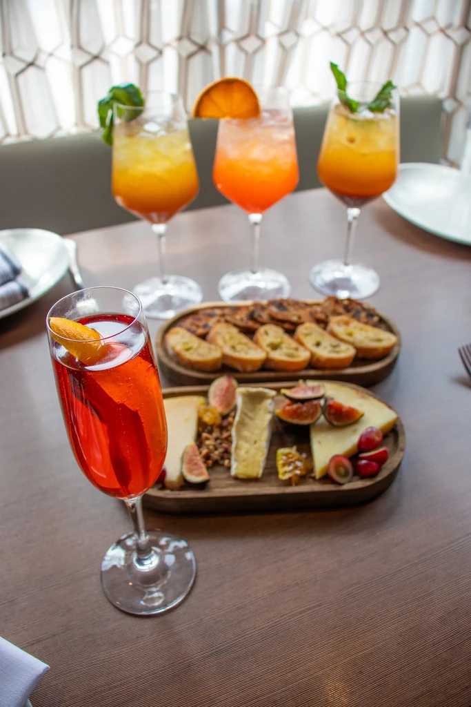 Cocktails, cheese platter, and crostini on a dark wooden table.