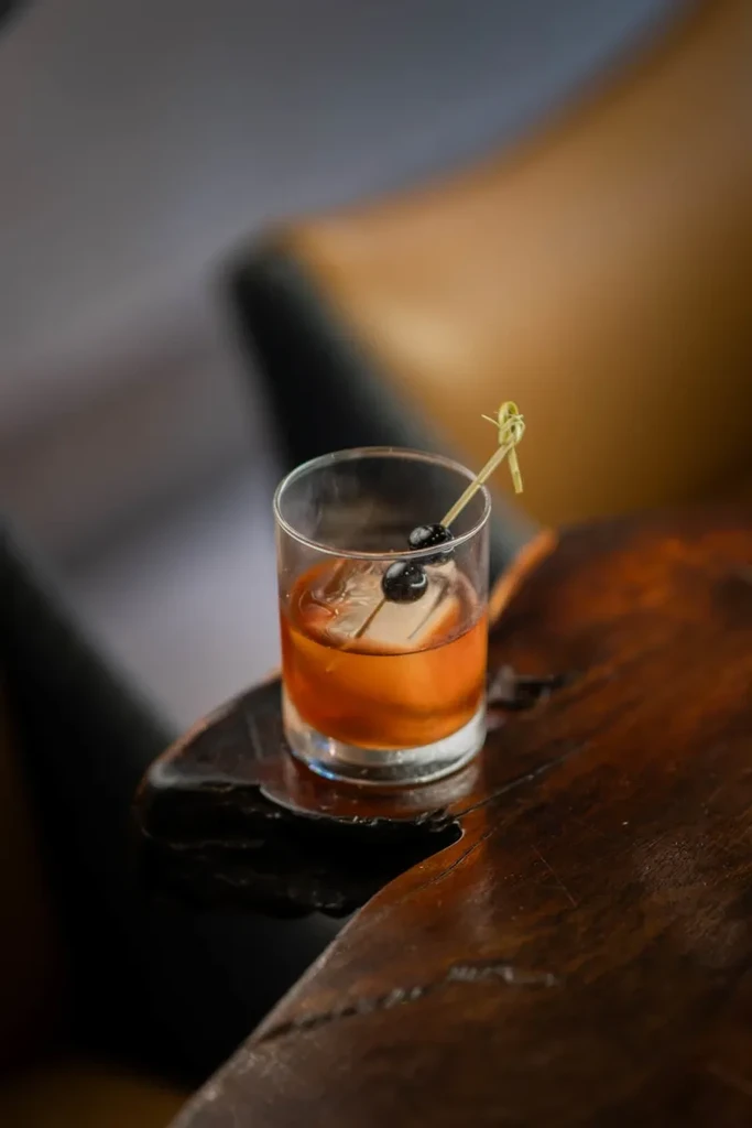 Amber cocktail with ice and cherries on a wooden table.