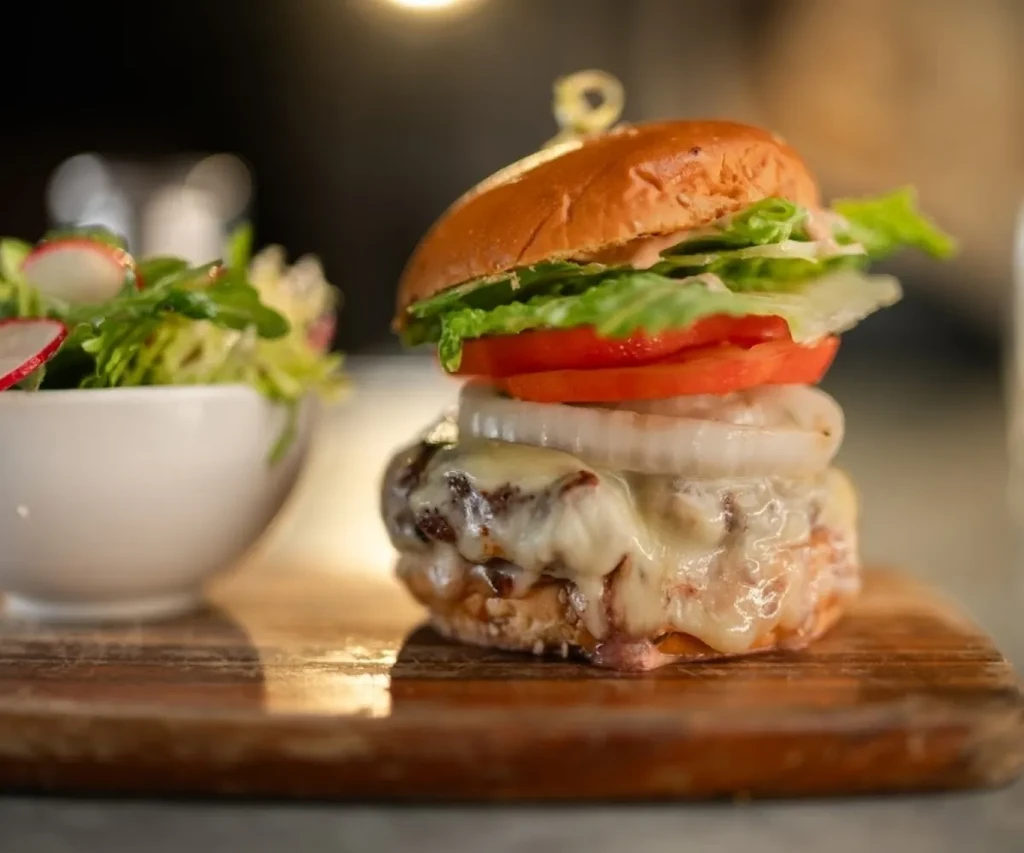 Close-up burger with melted cheese, fresh vegetables, and side salad.